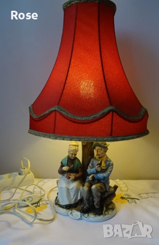 Лампа с фигурка на възрастна двойка, седнала на пейка под дърво. 