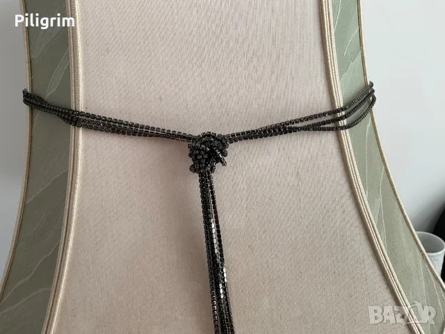 Сив камък в метална верижка от метални кристали.